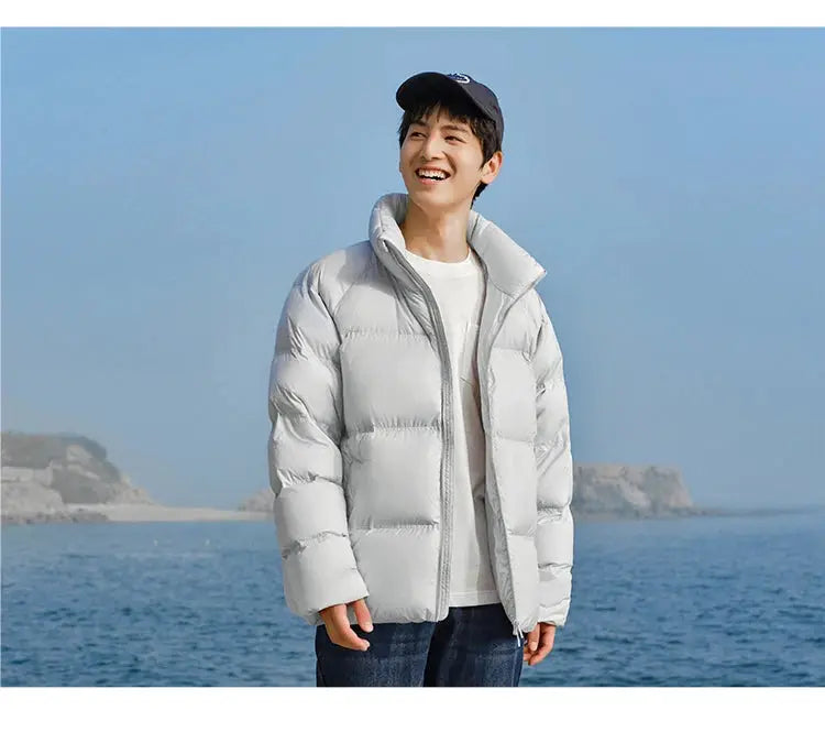 Unisex light gray Semir down jacket, short puffer coat with high collar, worn by model by the sea.
