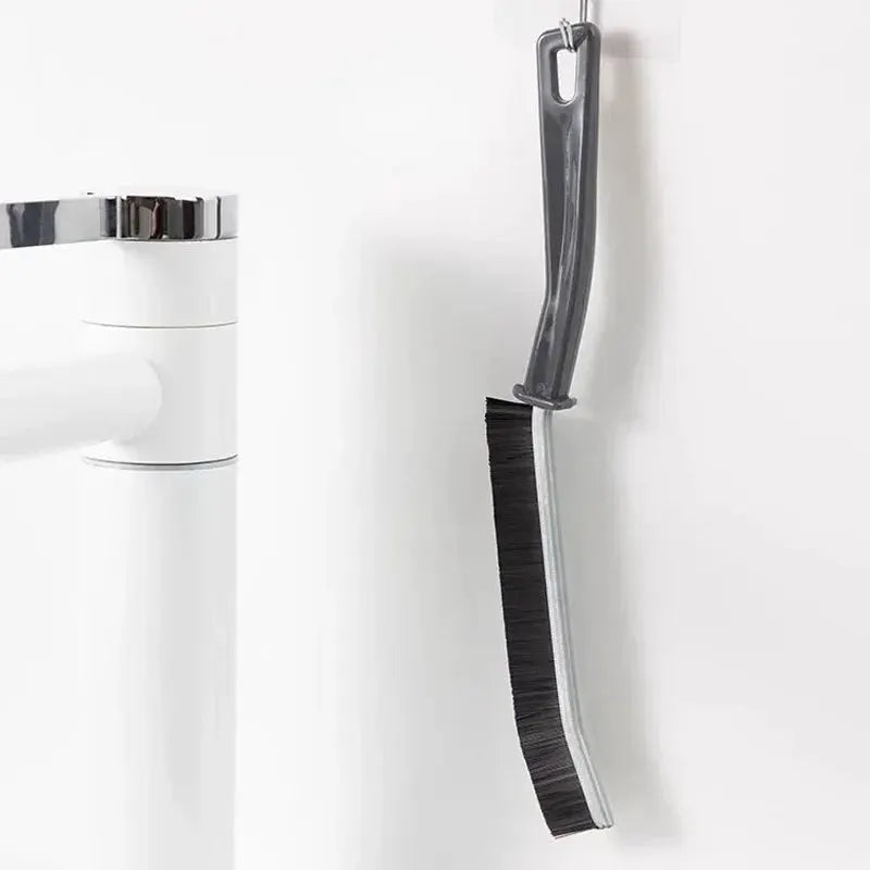 Simples Market grout cleaning brush with hard bristles, curved handle, hanging beside a toilet.
