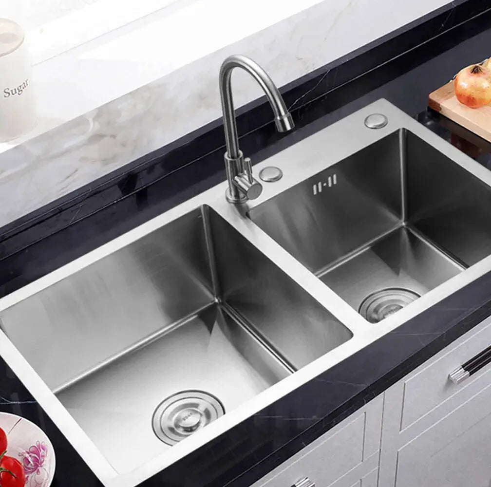 Stainless steel double-bowl drop-in kitchen sink with chrome faucet on a dark countertop.