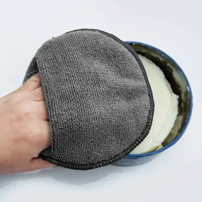 Round gray microfiber car detailing pad held in hand beside a blue wax can