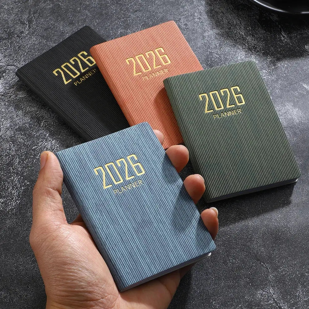 Four A7 mini pocket planners with textured ribbed covers in blue, green, pink, and black, gold 2026 lettering