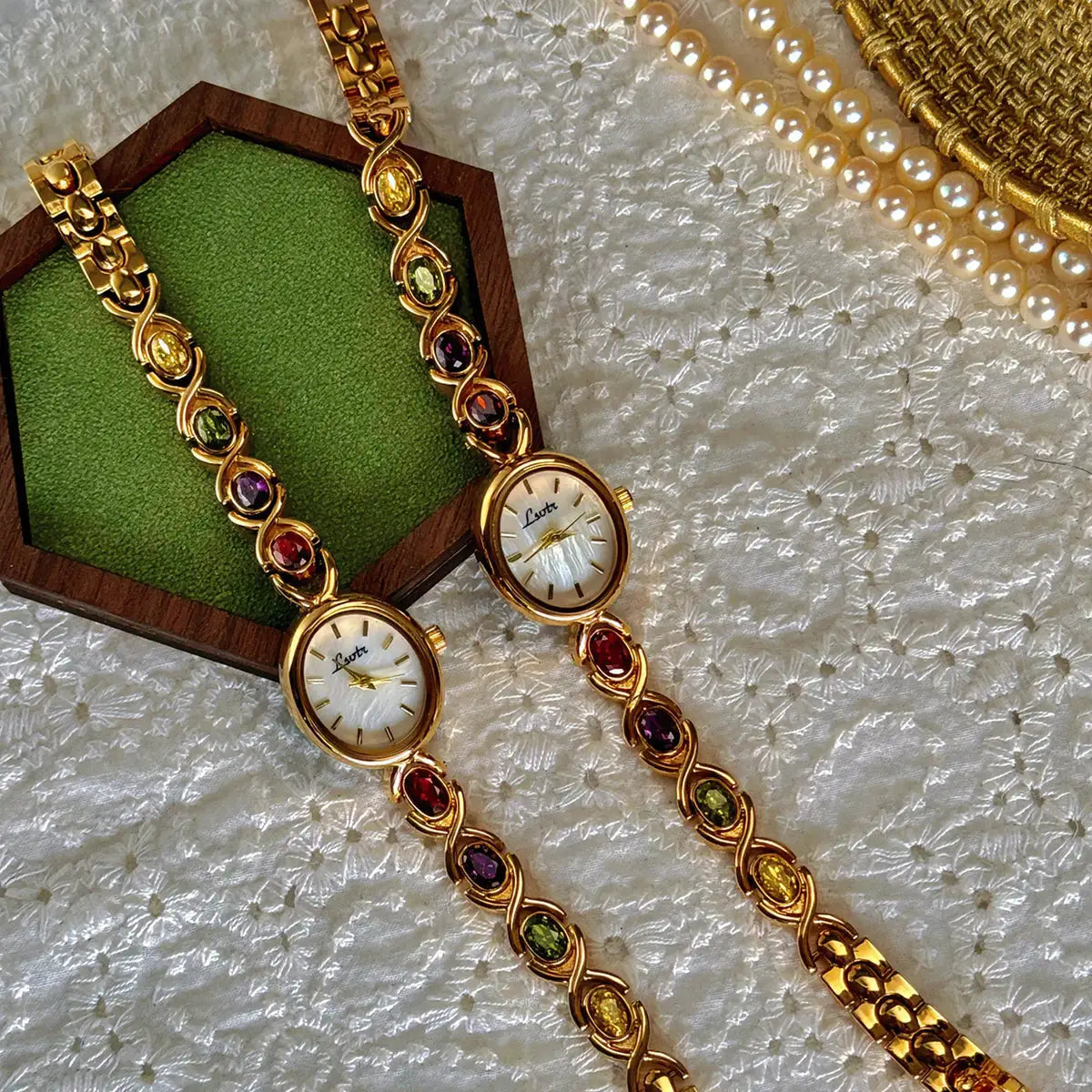 Two gold-tone luxury women's bracelet watches with colorful gemstones and oval mother-of-pearl dials, by Simples Market