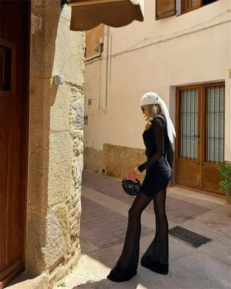Mozision black long-sleeve see-through jumpsuit with sheer panel legs, worn by a woman outdoors