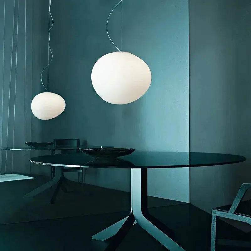 White glass ball pendant lights, set of two, suspended over a round glass dining table in a teal room