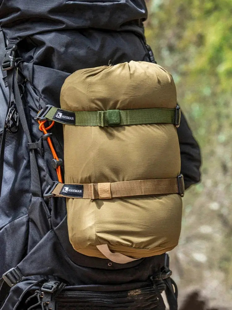 Outdoor luggage strap by Hikeman on a black hiking backpack securing a tan sleeping roll with green and brown buckles