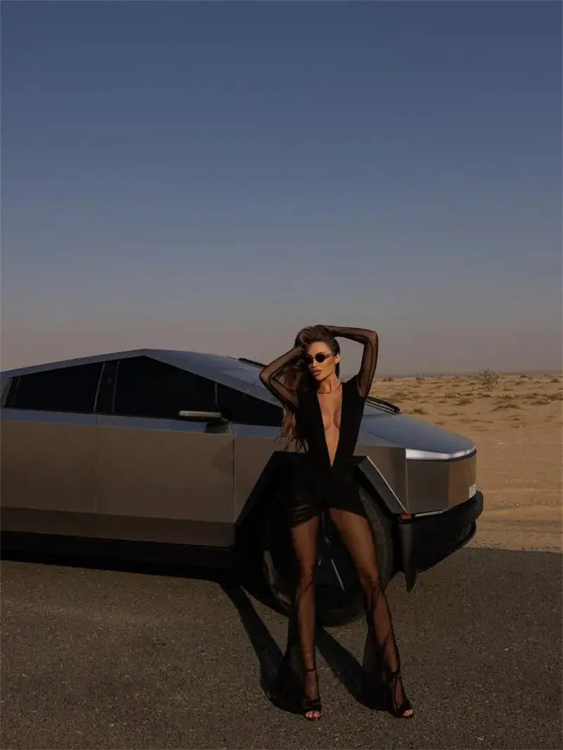 Mozision deep V-neck long-sleeve see-through jumpsuit by Simples Market; black, worn by a model beside a desert car