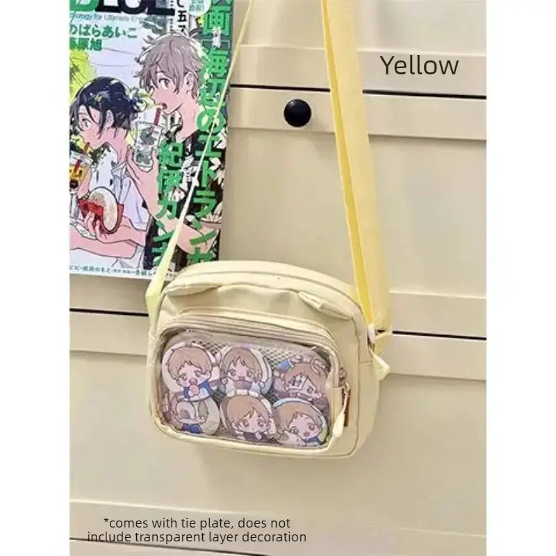 Itabag crossbody bag in beige with yellow strap and transparent front pocket displaying cartoon badges