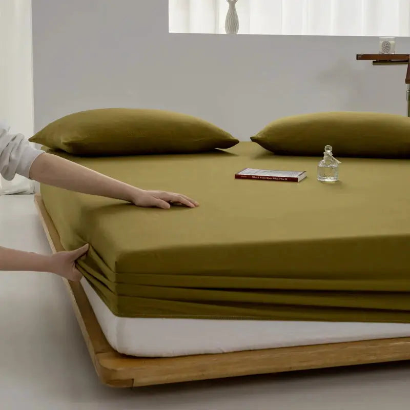 Soft cotton fitted sheet in olive green with elastic edges on a bed with matching pillows.