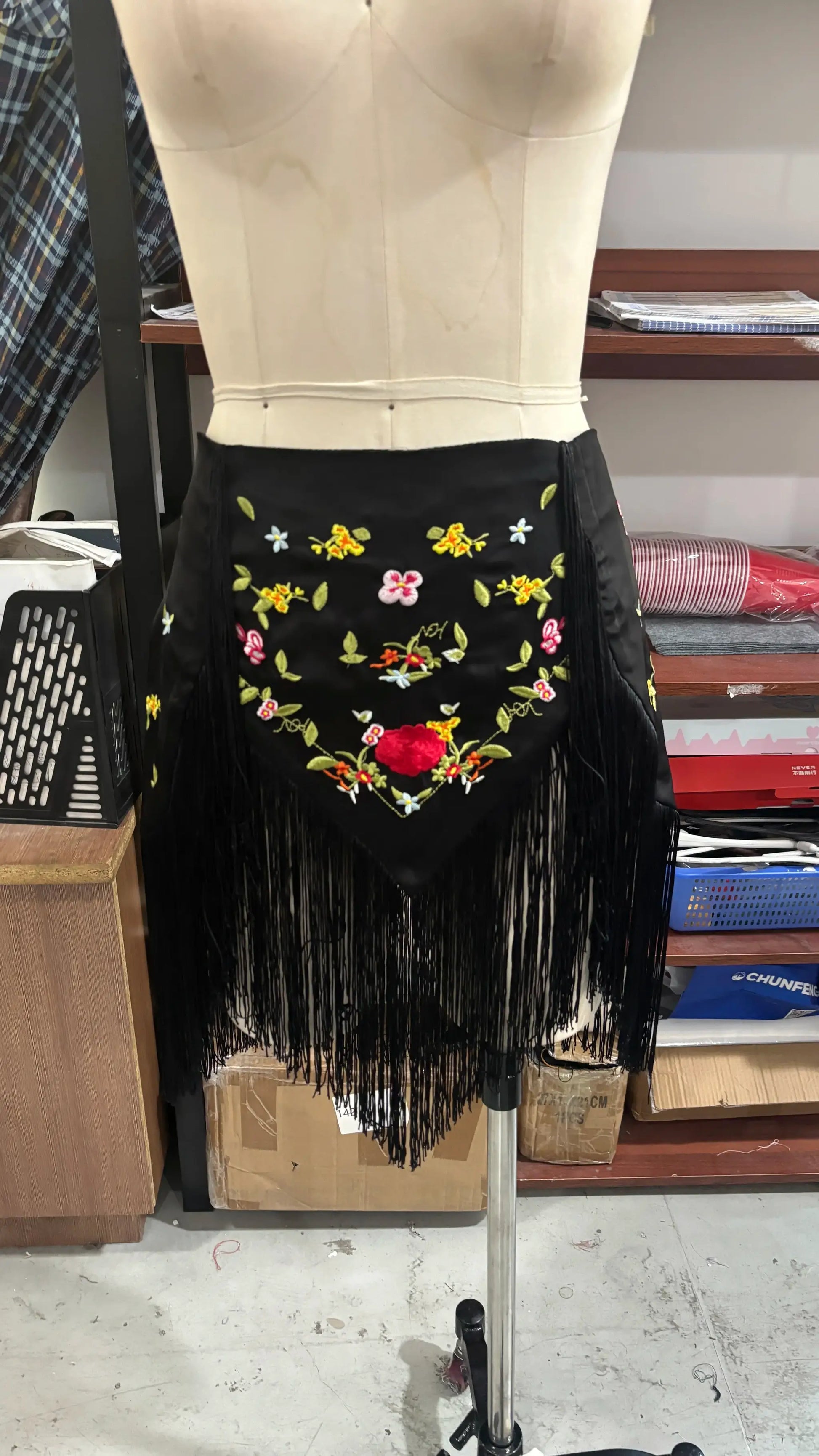 Black embroidered fringe skirt on a mannequin with colorful floral embroidery and long fringe hem.
