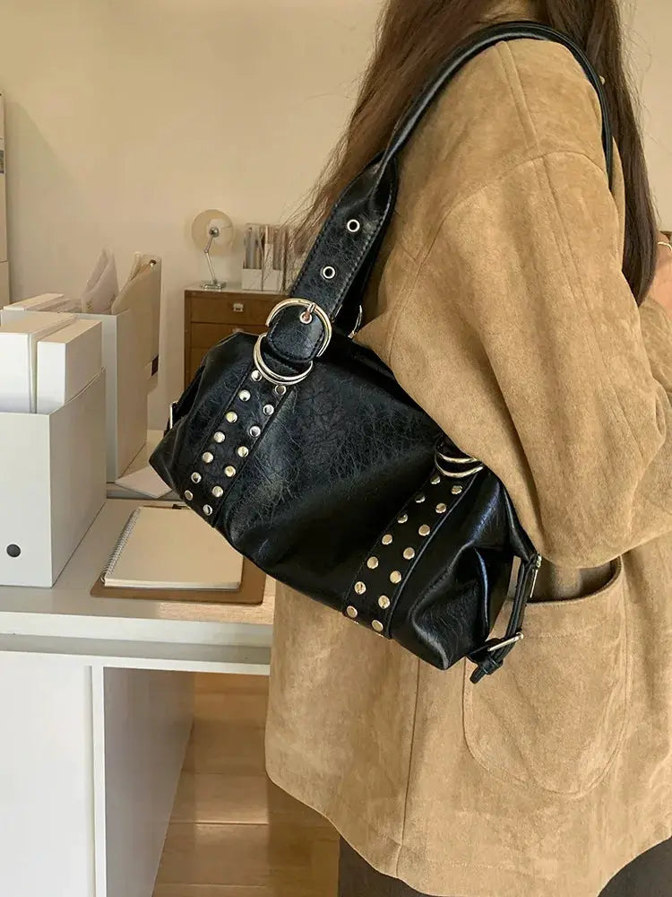 Black PU leather shoulder bag with silver studs and rivets, carried by a woman in a tan coat.