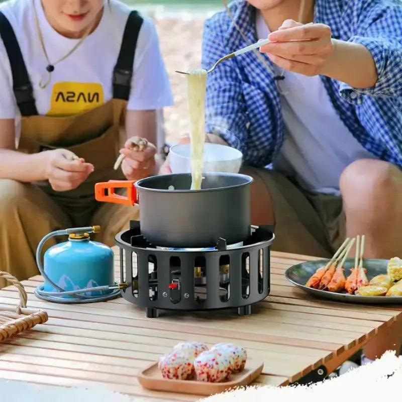 Portable camping stove by Simples Market with black burner, orange pot handle, blue fuel canister