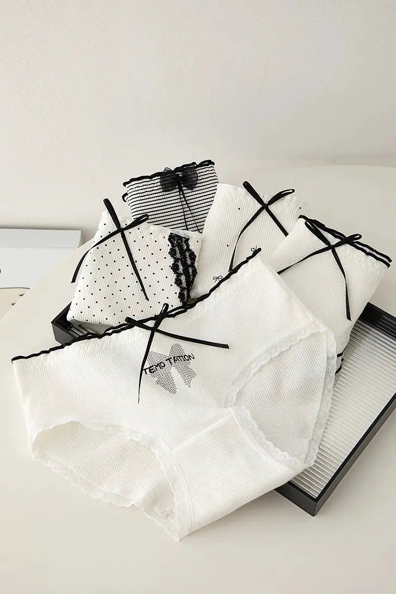 White lace panties with black ribbon bows, set of five displayed on a tray
