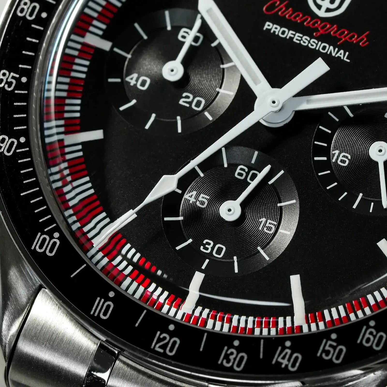 Chronograph watch dial close-up with black face, white hands, three subdials, and red-white tachymeter bezel.