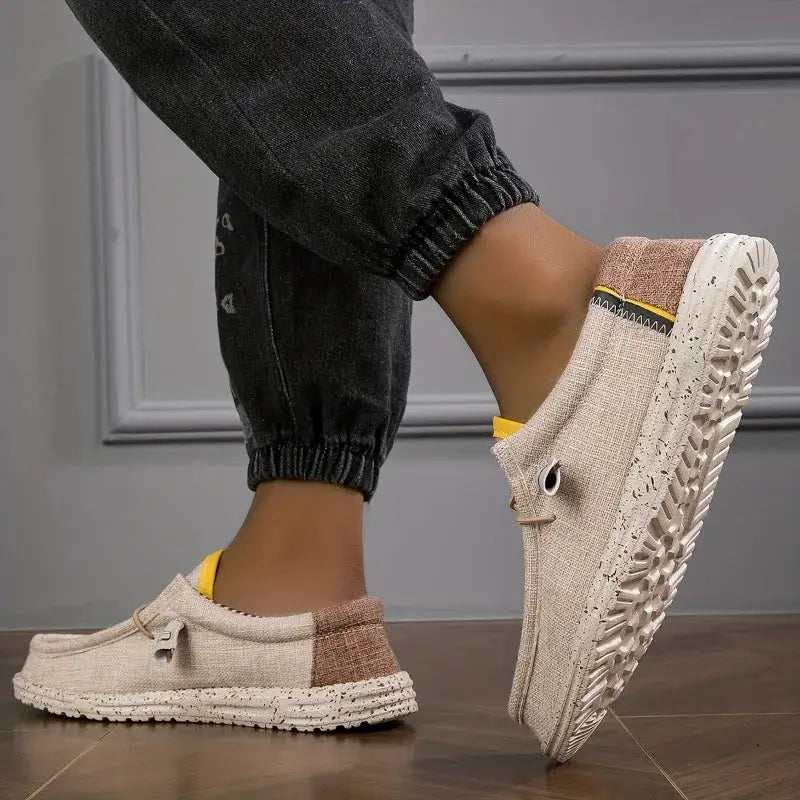 Men's beige canvas loafers with brown heel patch and yellow pull tab; textured rubber sole.