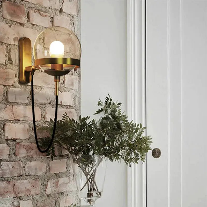 Simples Market modern glass ball wall lamp with brass finish, glass globe shade and black cord on brick wall