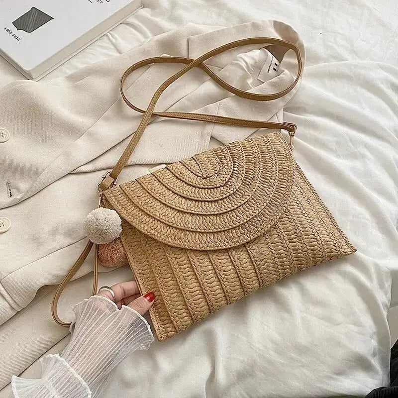 Handmade straw beach crossbody bag with envelope flap, natural beige weave, tan strap, and fluffy pom pom charm