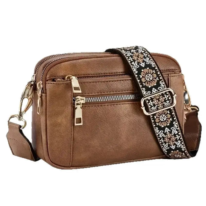 Crossbody square bag, brown leather-like finish with gold zippers and an adjustable decorative woven floral strap