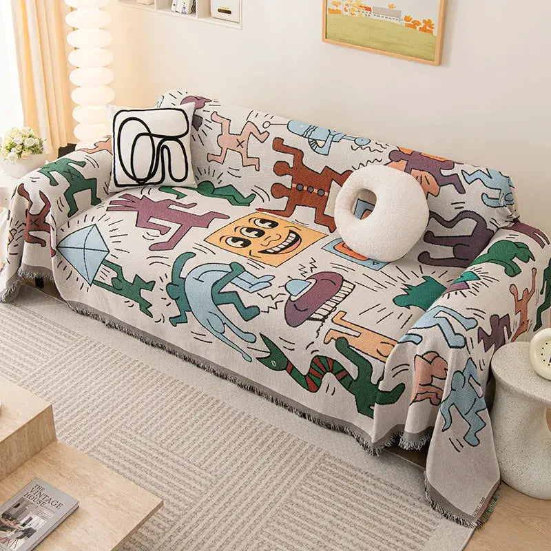 Cream sofa throw blanket with colorful abstract figures and fringe on a beige sofa