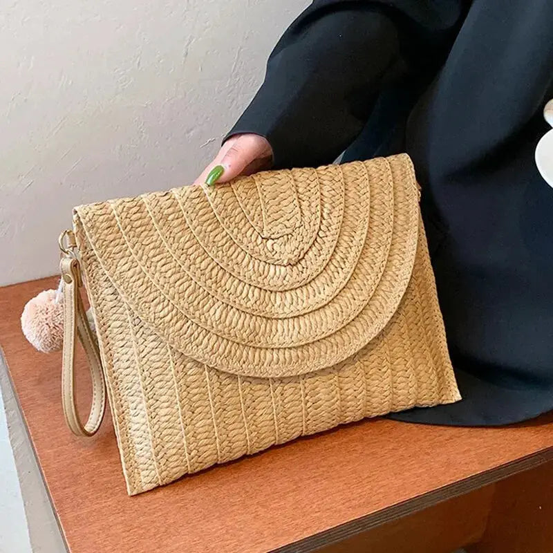 Handmade straw crossbody bag with envelope flap, natural woven texture and pink pom-pom charm