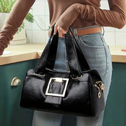 Women black leather top-handle bag with gold square buckle and roomy interior.