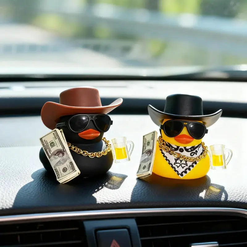 Two cowboy rubber duck car ornaments on the dashboard, black and yellow ducks with hats, sunglasses, and gold chains.