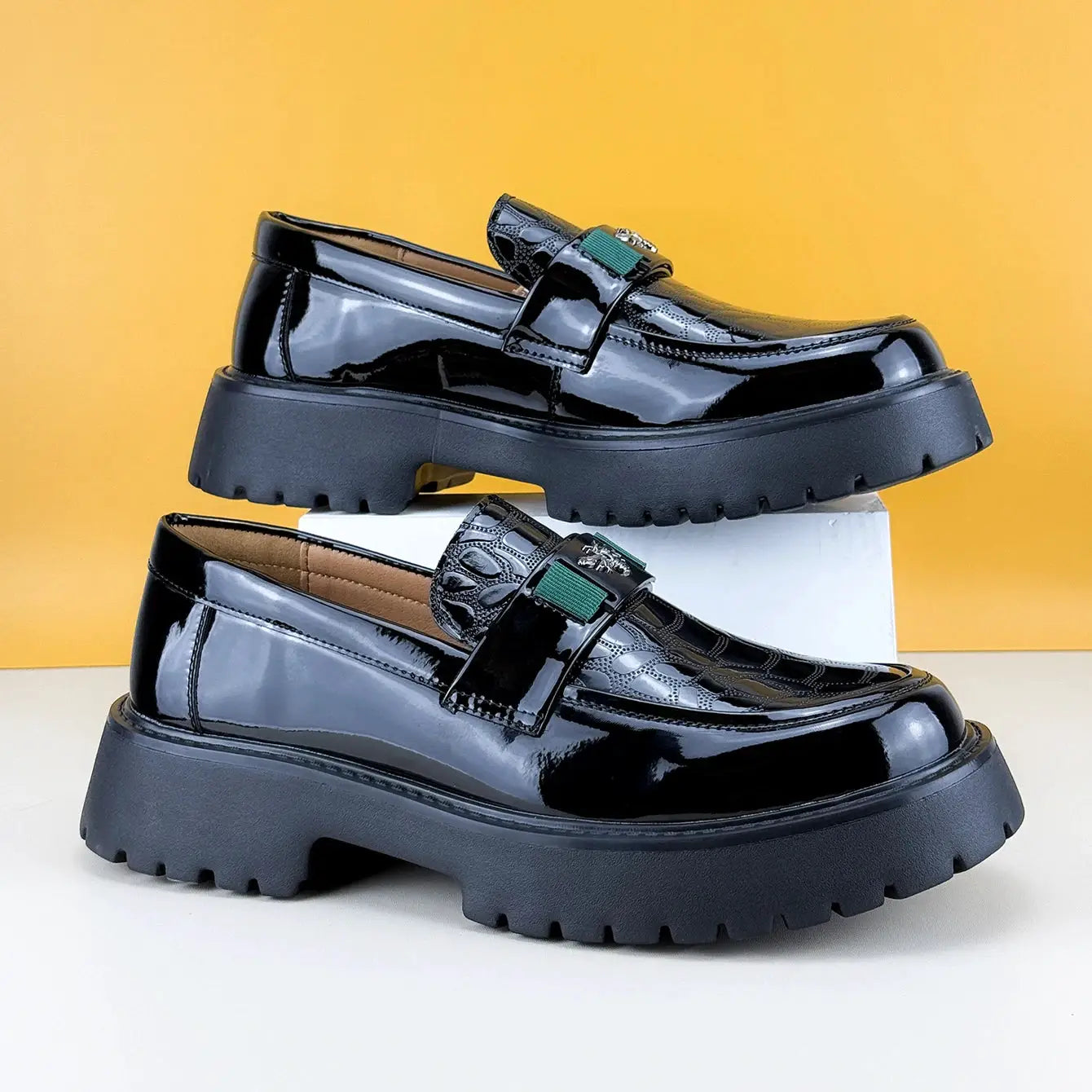 Pair of men's black patent leather loafers with chunky platform soles and green strap accents.