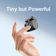 Mini 2K car dash camera in black with orange power button held between fingers against a blue sky