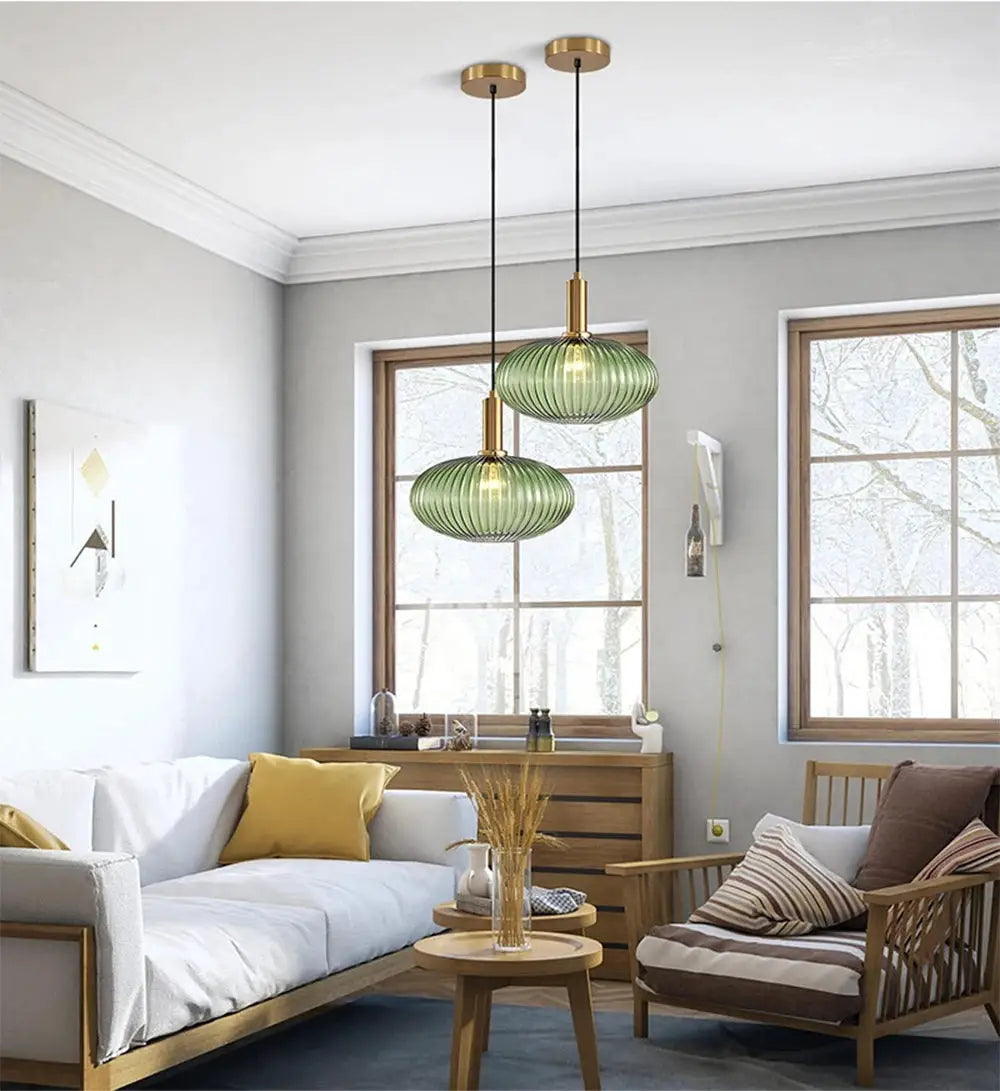 Nordic glass pendant lights, two green ribbed glass shades with brass fittings, hanging in a modern living room.