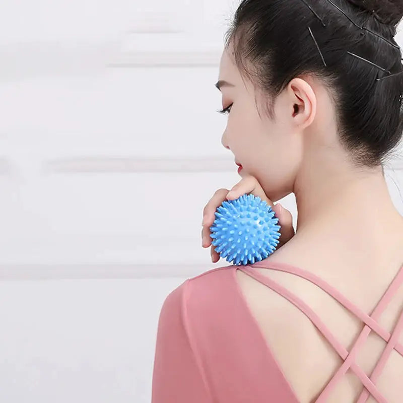 Fascia ball massage blue spiky ball for neck and shoulder relief, held in hand by a woman wearing a pink top