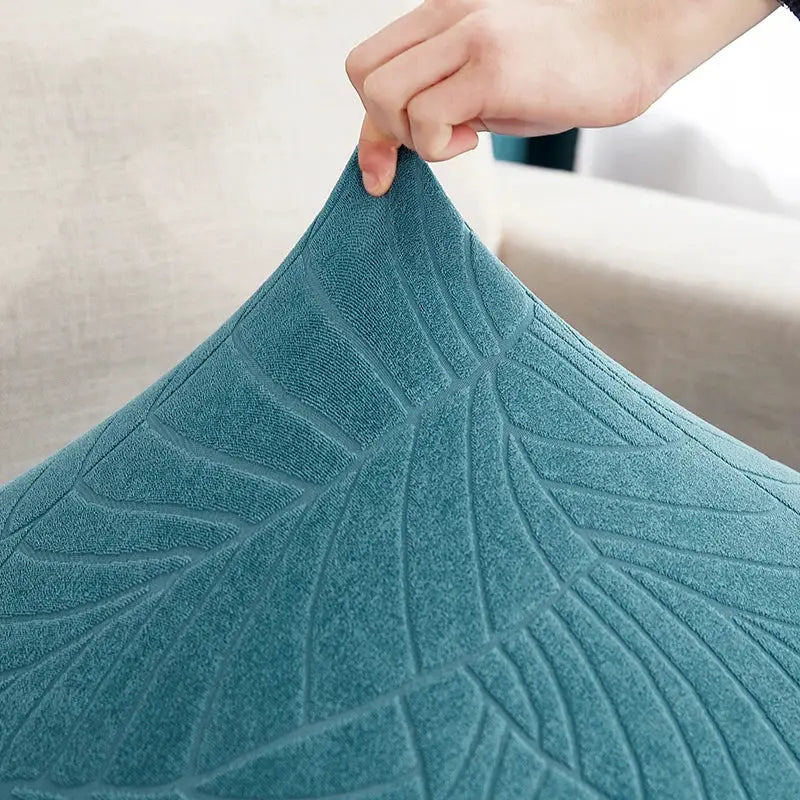 Teal waterproof stretch sofa cushion cover being stretched by hand on a couch