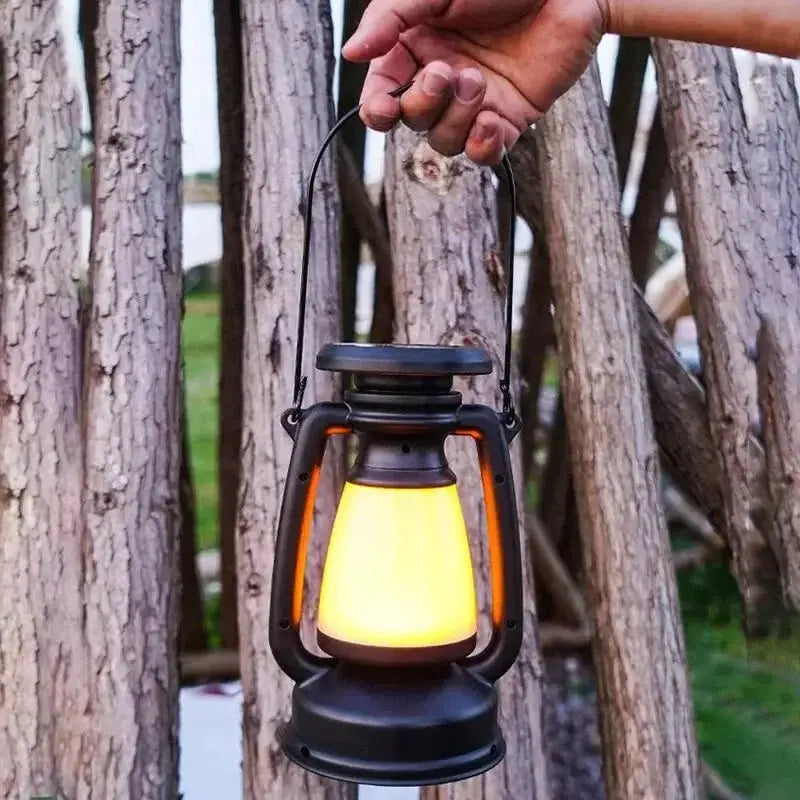 Charging lantern by Simples Market with warm yellow glow, black metal frame and orange handles.