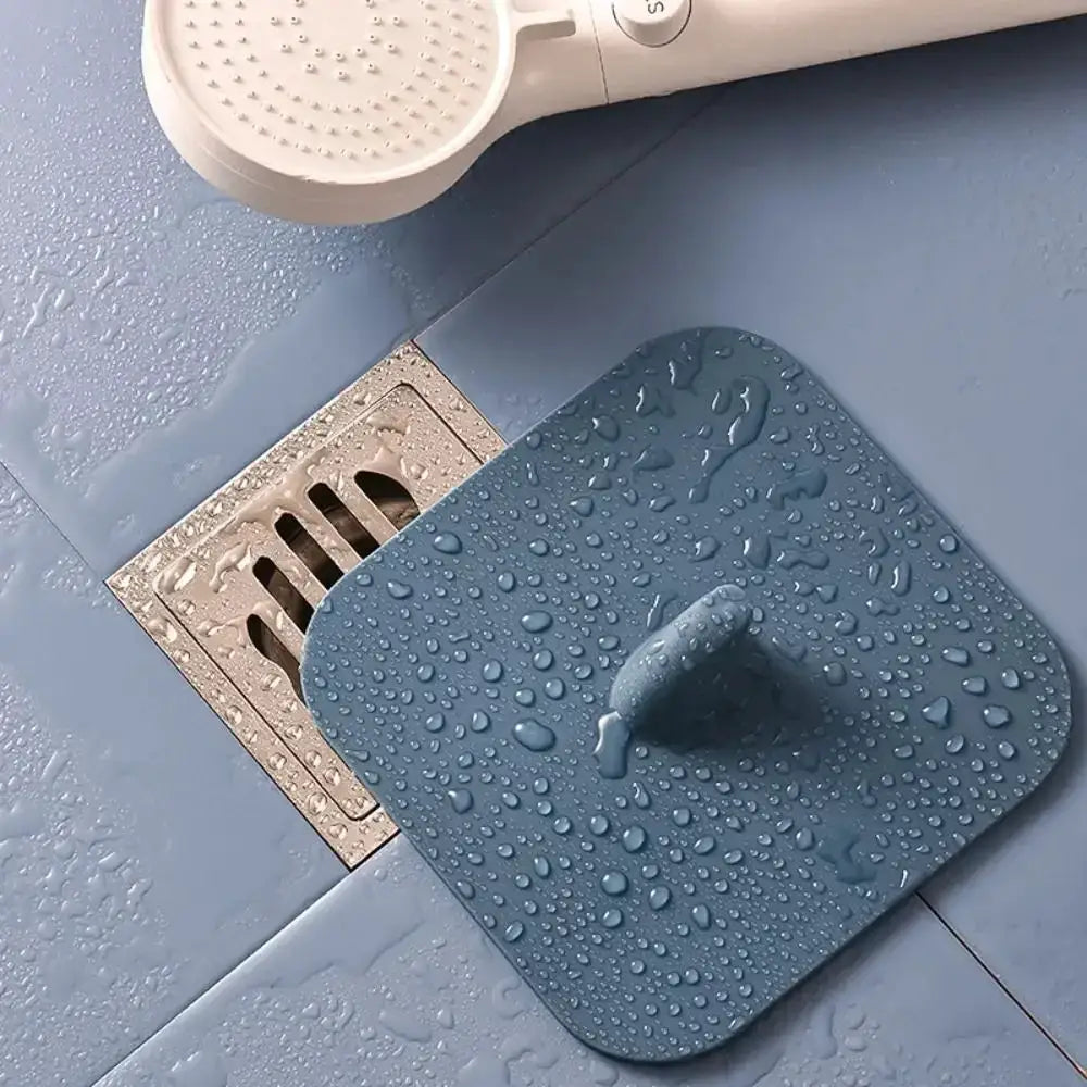 Blue silicone bathroom drain pad placed over a floor drain with water droplets on its surface.