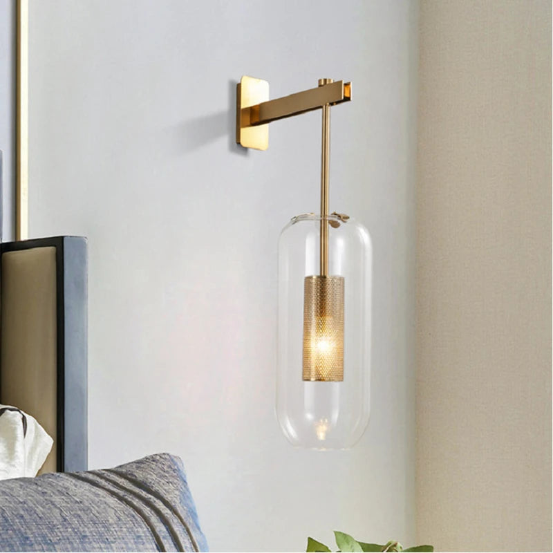 Modern glass wall light sconce with clear cylindrical shade and brass base, wall-mounted bedside lamp