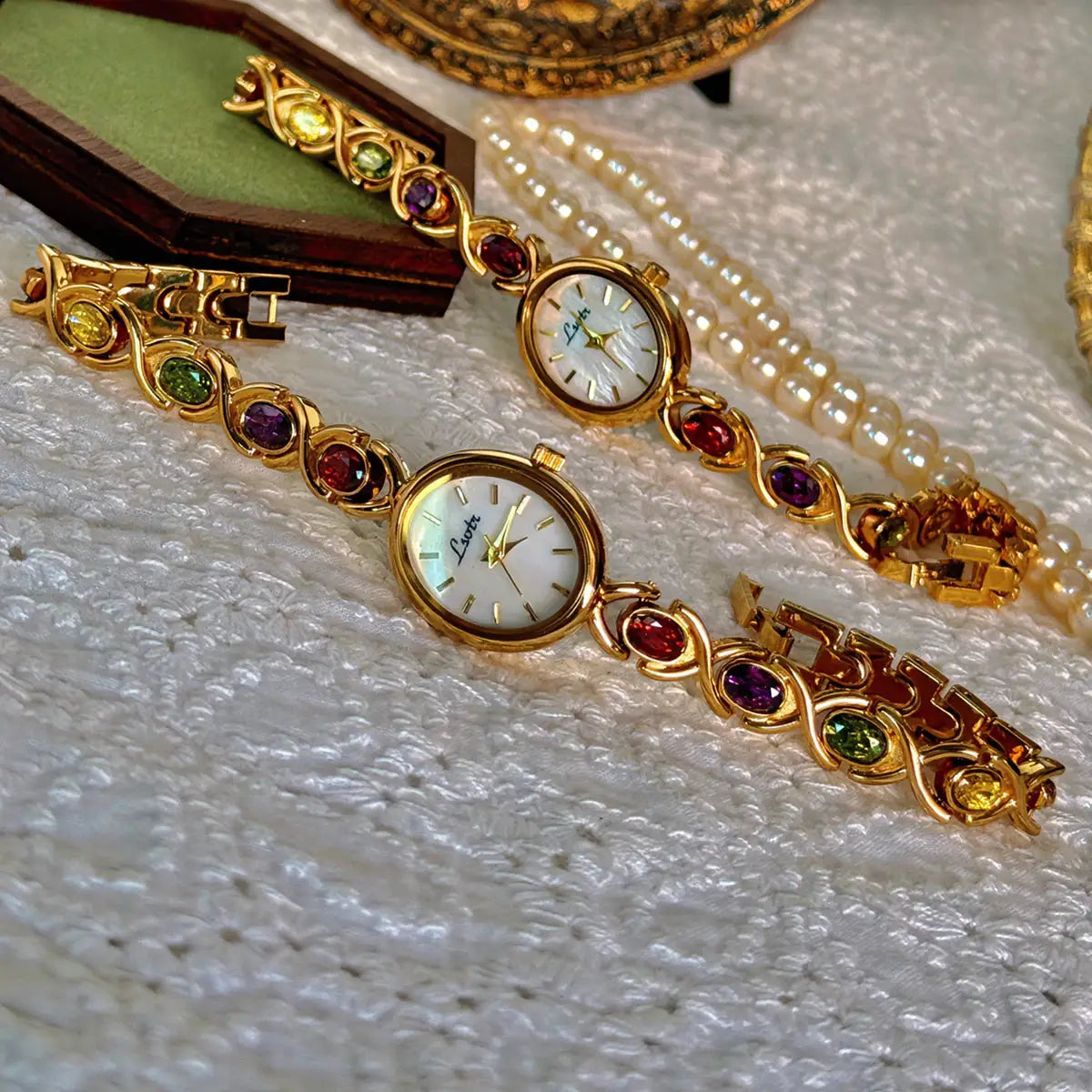2 gold-tone women's watches with round mother-of-pearl dials and colorful gemstone bezels