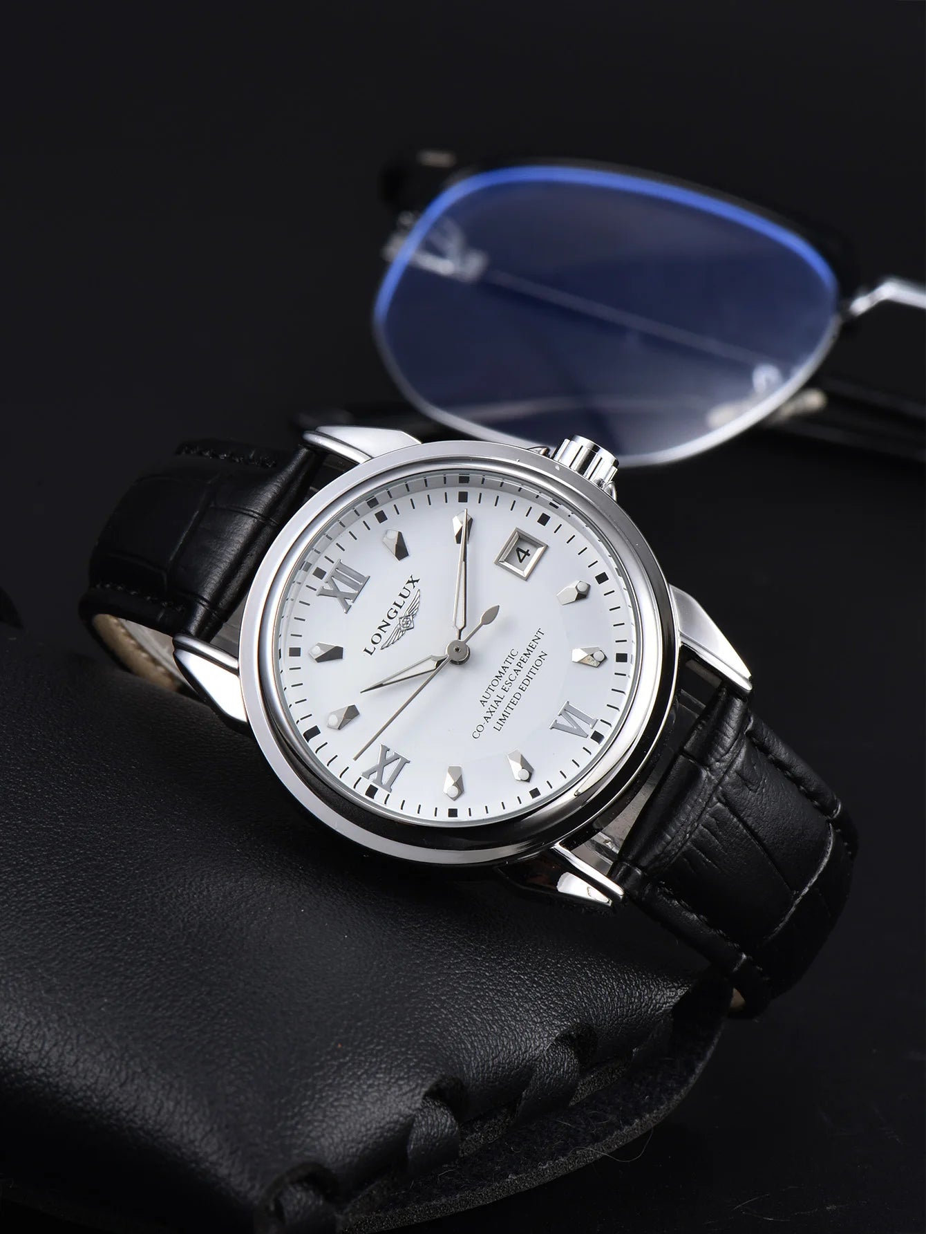 Men's automatic wristwatch with silver case, white dial, Roman numerals, date window, and black leather strap.