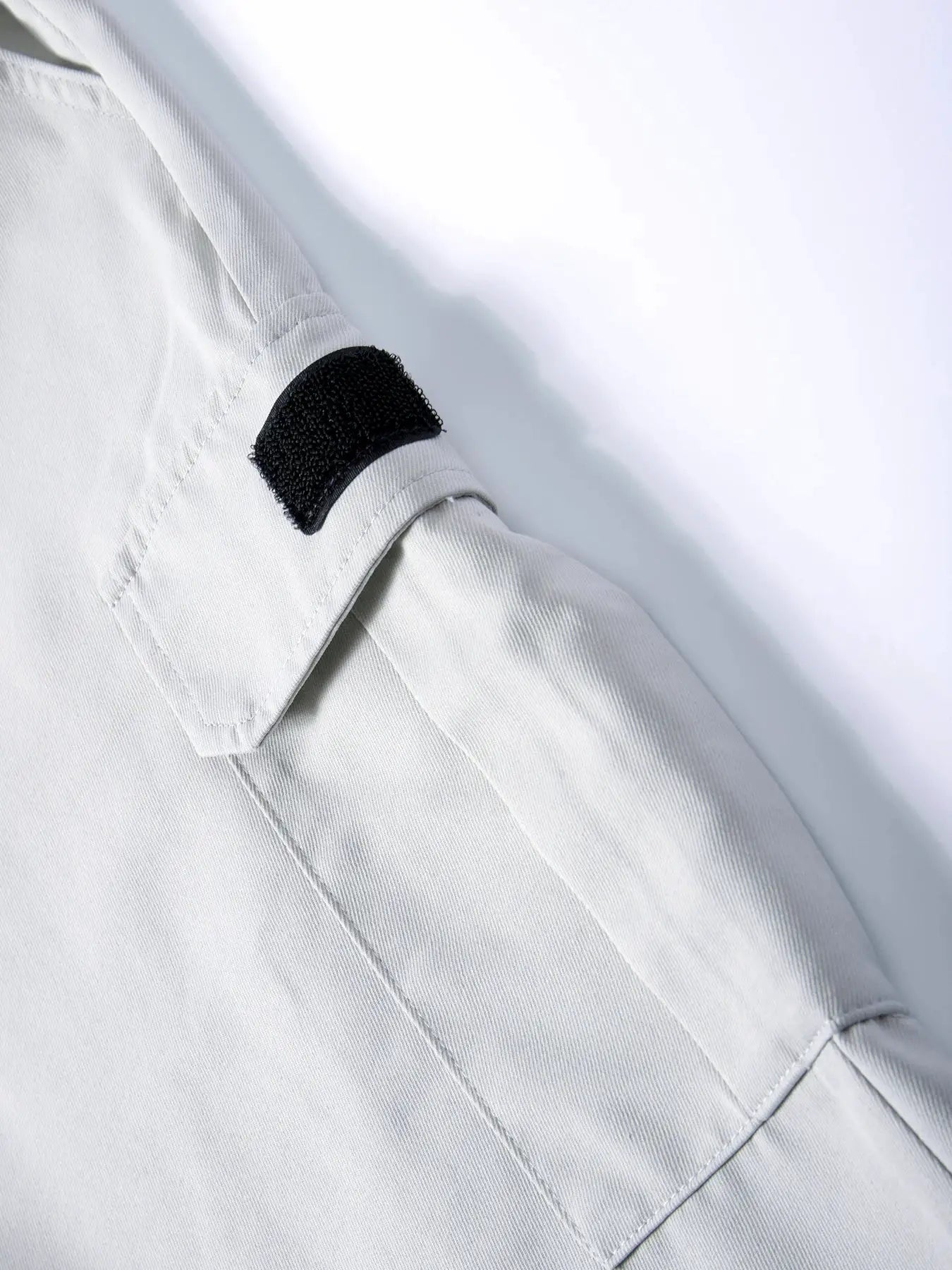 Spring men's cargo pants in light gray cotton twill, close-up of pocket with black Velcro closure for secure fit.