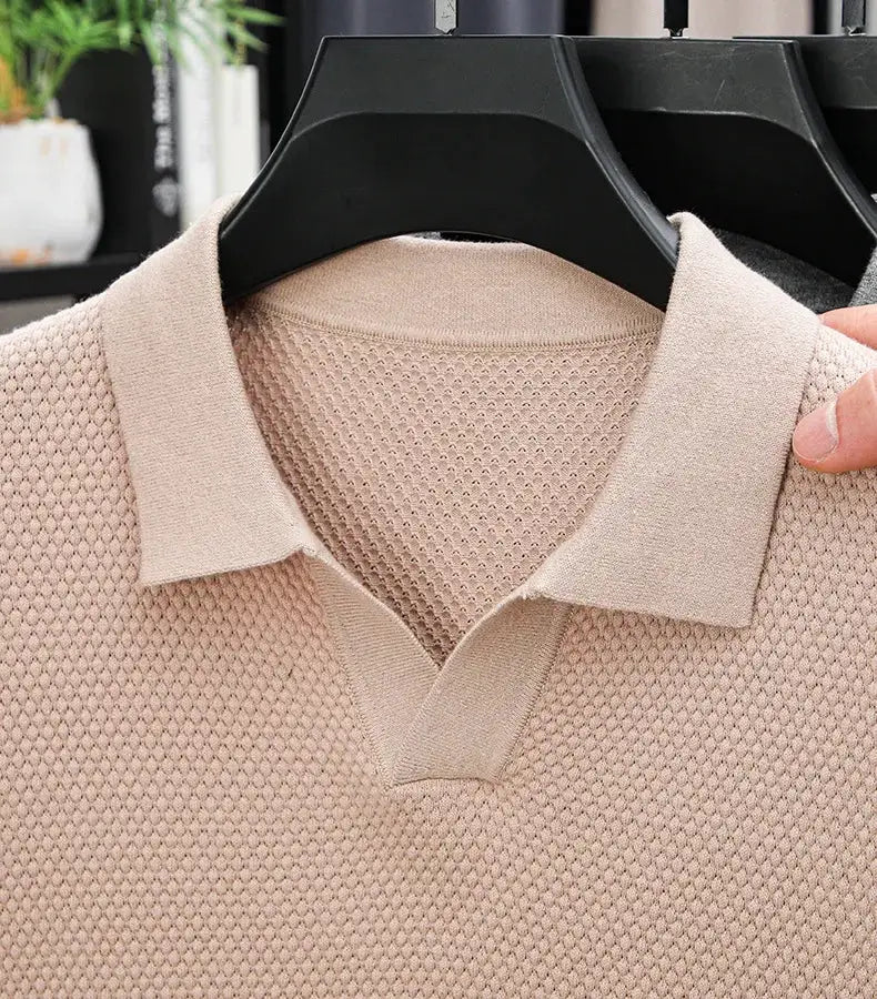 Beige knitted polo shirt on hanger; short sleeves, polo collar, textured knit fabric.
