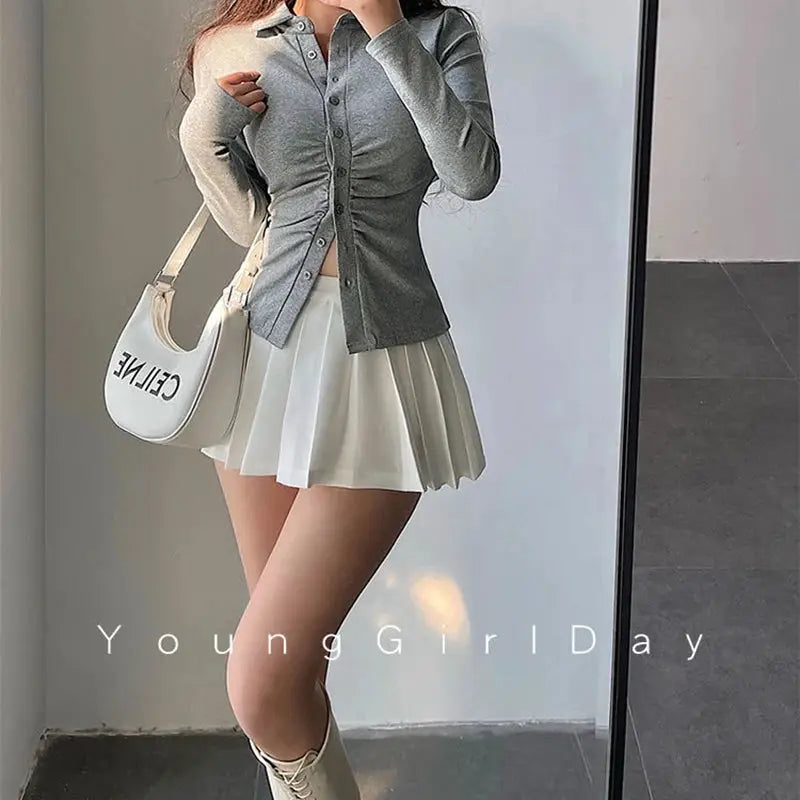 White pleated mini skirt with built-in shorts, high-waist A-line for women, shown with a gray top and a Celine bag