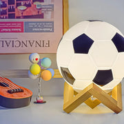 Soccer ball night light on a wooden X-shaped stand; 14 cm, white with dark panels, glowing desktop decoration.