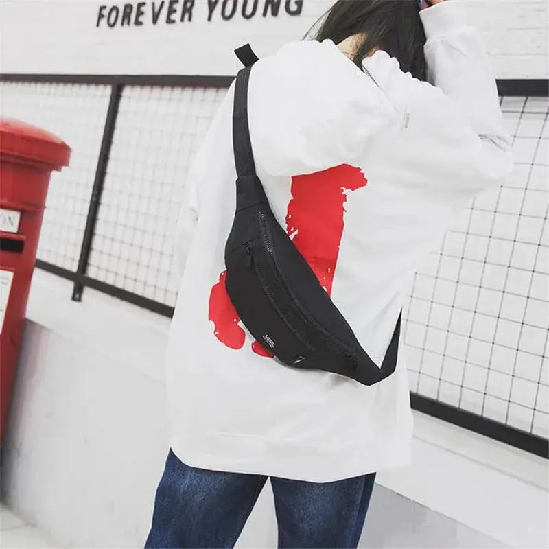 Black fanny pack crossbody belt bag worn by person in white hoodie and blue jeans
