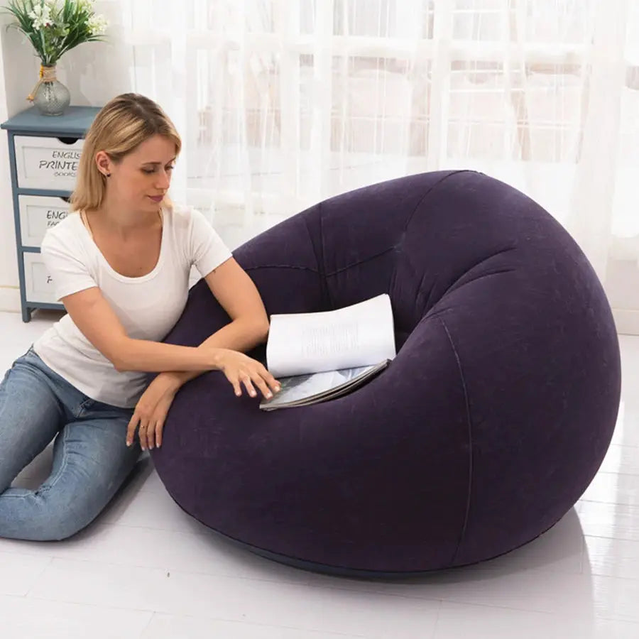 Large purple PVC bean bag lounger sofa chair by Simples Market, shown with a person reading indoors.