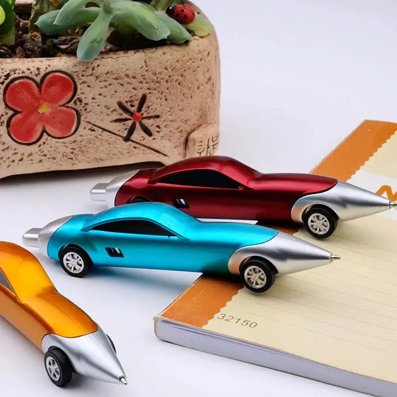 Car-shaped ballpoint pens in blue, red, and orange; three pieces by Simples Market on a notebook.