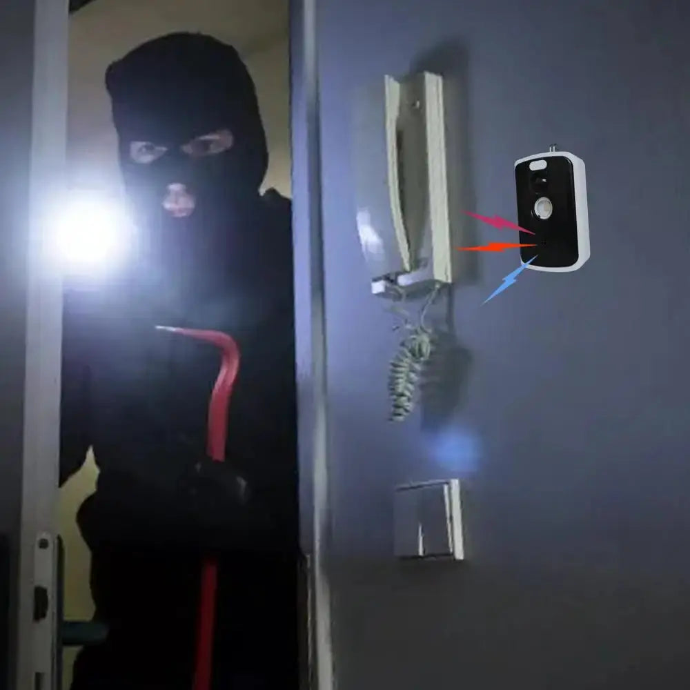 Wireless PIR infrared alarm sensor mounted outdoors beside a door on a gray wall; intruder visible in frame.