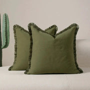 Boho pillow covers in olive green with tassel fringe on a beige sofa; set of two