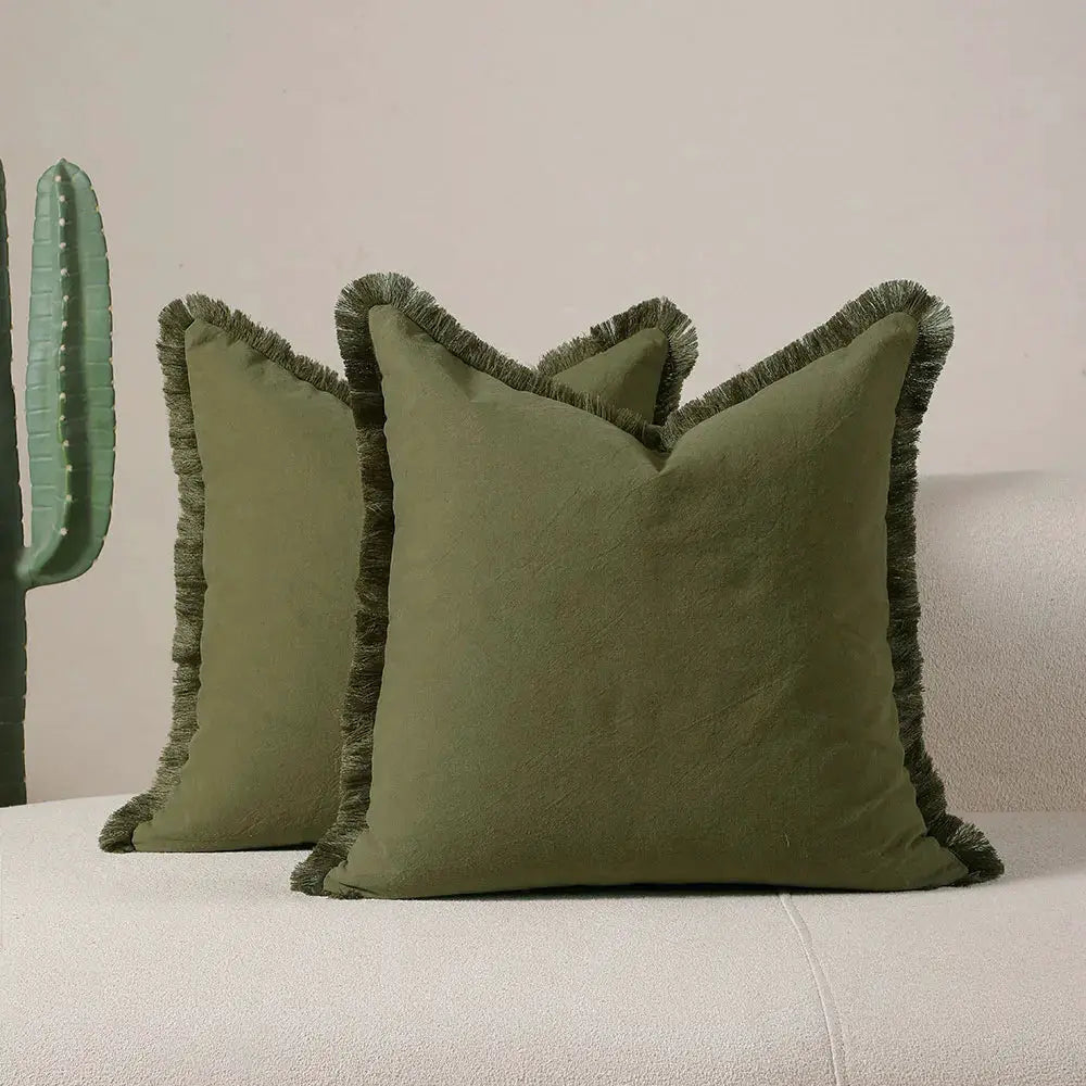 Boho pillow covers in olive green with tassel fringe on a beige sofa; set of two