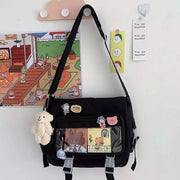 Simples Market black canvas crossbody bag with front clear panel, cartoon patches, and a plush teddy keychain.