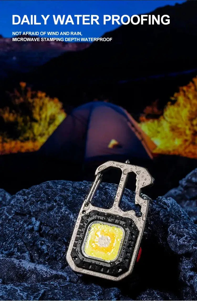 COB Keychain Work Light by Simples Market with carabiner, metal body and yellow LED panel in an outdoor camping scene