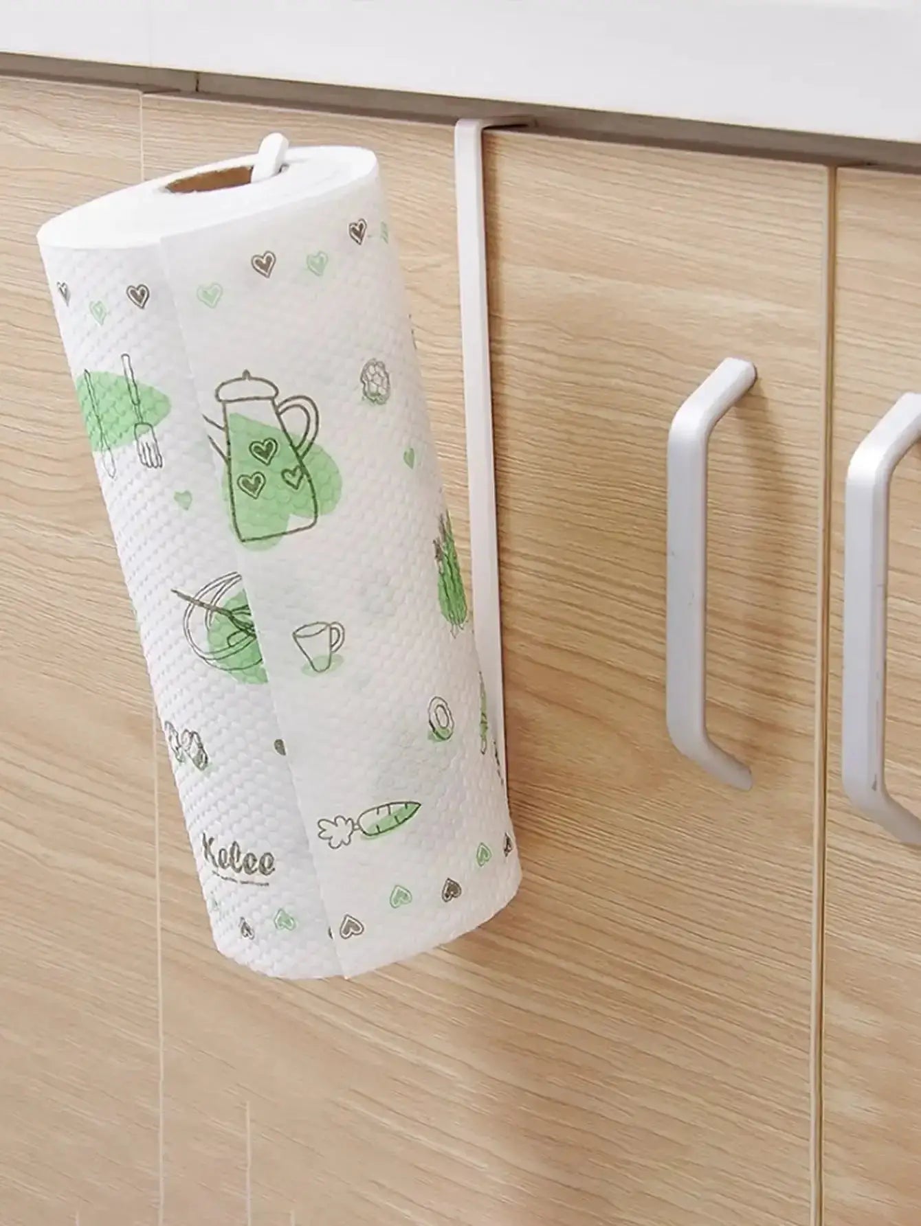 Paper towel holder hanging rack in white plastic mounted on a wood cabinet, holding a patterned paper towel roll.
