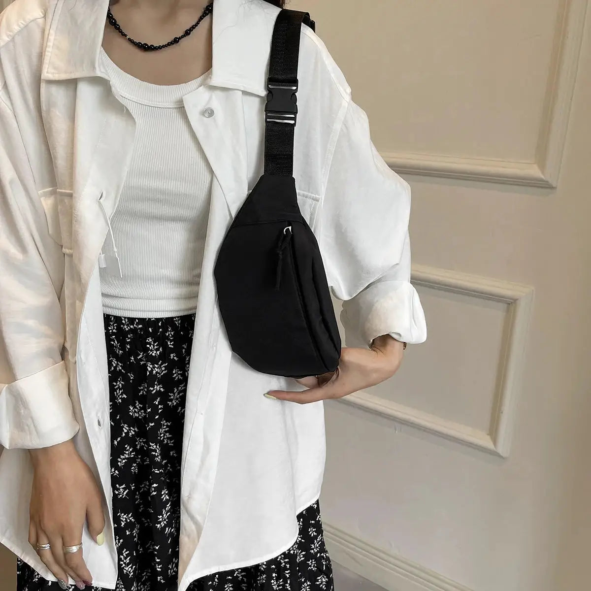 Black nylon fanny pack with an adjustable strap worn crossbody on a white outfit.