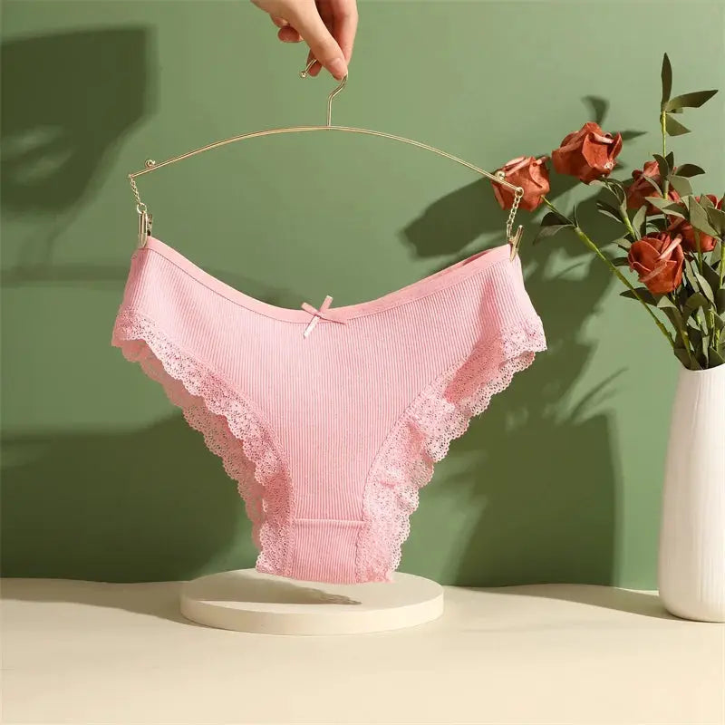 Pink lace-trim cotton briefs with ribbed fabric and bow, displayed on a hanger.